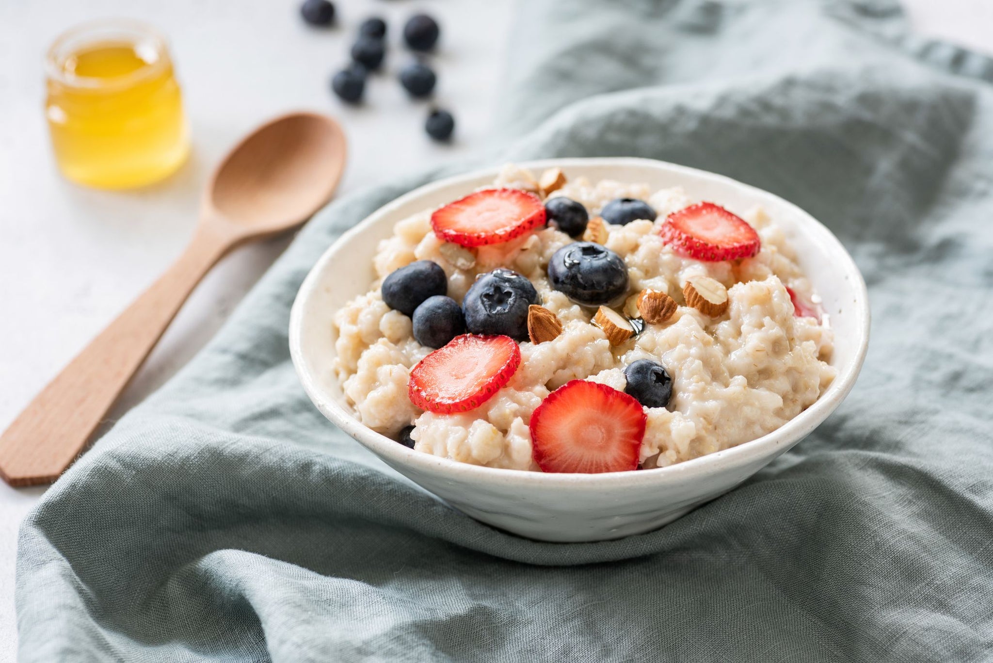 Bowl of creamy oatmeal topped with strawberries, blueberries and chopped almonds, with a jar of honey in the background